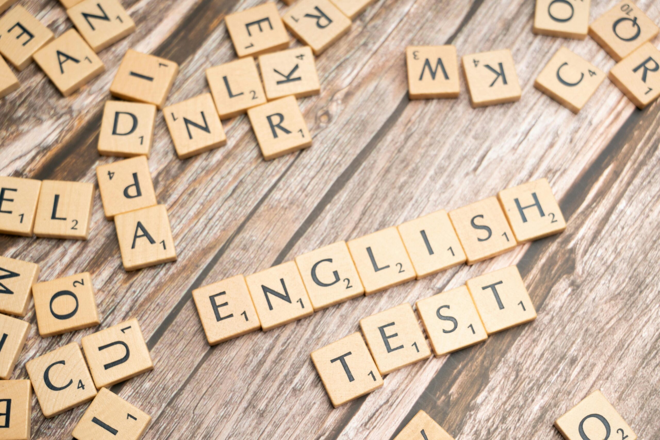 Wooden Scrabble tiles spelling out 'English Test' on a wooden background, ideal for language exam themes.