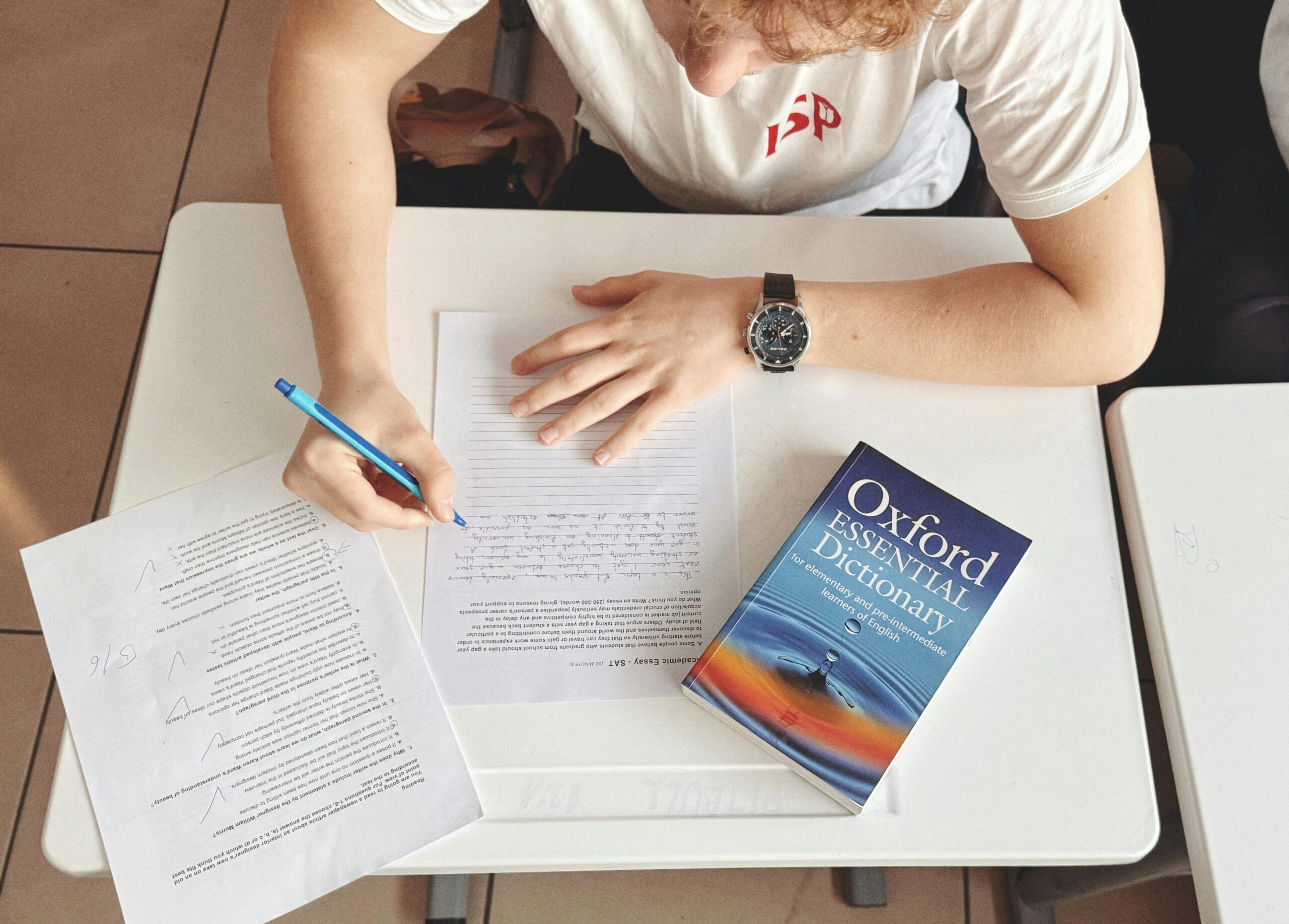 Student writing test using paper and Oxford dictionary on desk in classroom