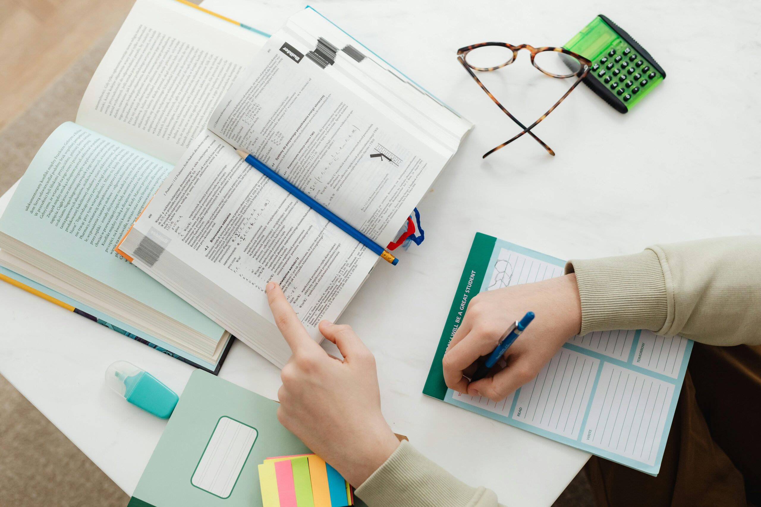 Top view of a student studying with open books, a calculator, and a notebook on a desk.